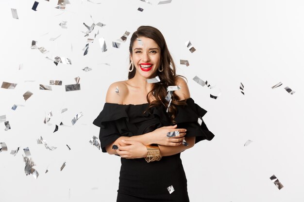 Happy woman celebrating winter holidays, smiling cheerful, partying on New Year with confetti, standing over white background.