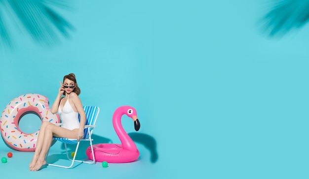 Happy woman chilling in lounge chair near flamingo rubber ring on blue copy space background