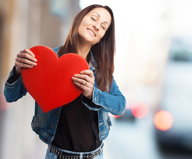 Счастливая женщина в джинсовой куртке с гигантским сердцем