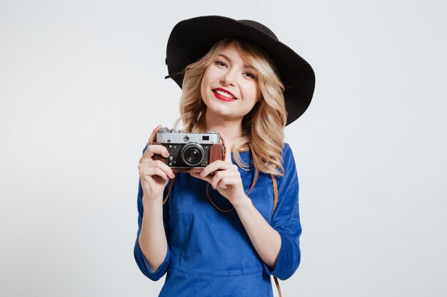 Happy woman dressed in blue dress wearing hat holding camera