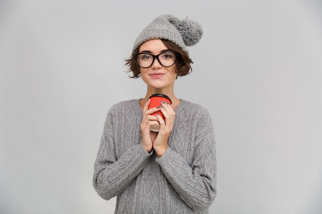 Happy woman dressed in sweater and warm hat drinking coffee.