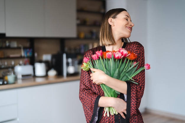 Happy woman enjoy bouquet of tulips Housewife enjoying a bunch of flowers and interior of kitchen Sweet home Allergy free