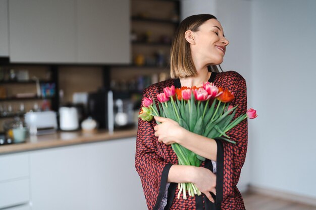 Счастливая женщина наслаждается букетом тюльпанов Домохозяйка наслаждается букетом цветов и интерьером кухни Милый дом Без аллергии