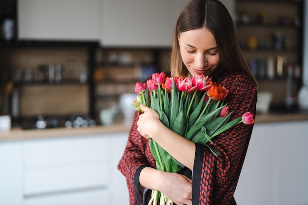 Donna felice godere bouquet di tulipani casalinga godendo di un mazzo di fiori e interni della cucina sweet home senza allergie