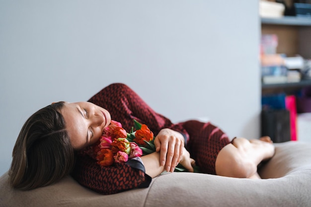 행복한 여자는 튤립 꽃다발을 즐긴다 편안한 빈백에서 휴식을 취하면서 꽃 다발을 즐기는 주부 스위트 홈 알레르기 없음