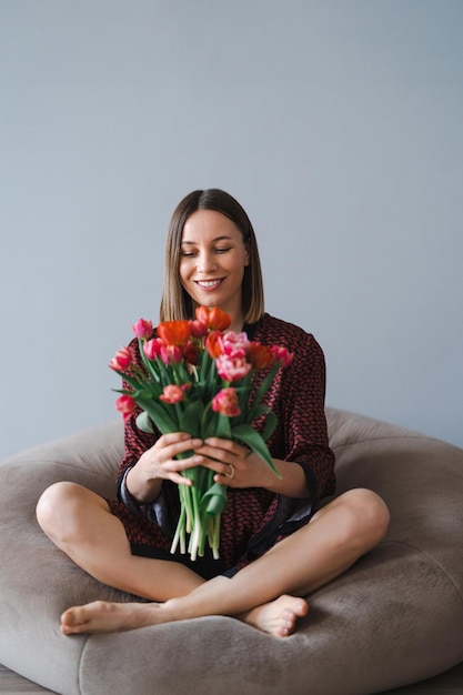 Счастливая женщина наслаждается букетом тюльпанов Домохозяйка наслаждается букетом цветов, отдыхая на удобном мешочке с фасолью Милый дом Без аллергии