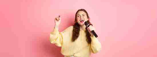 Free photo happy woman enjoying singing karaoke holding mic and looking aside dancing and having fun standing o