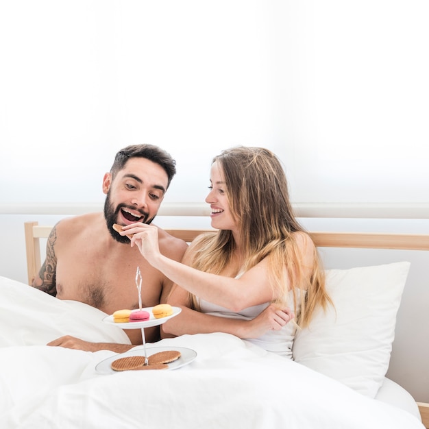 Free photo happy woman feeding biscuit to her boyfriend on bed