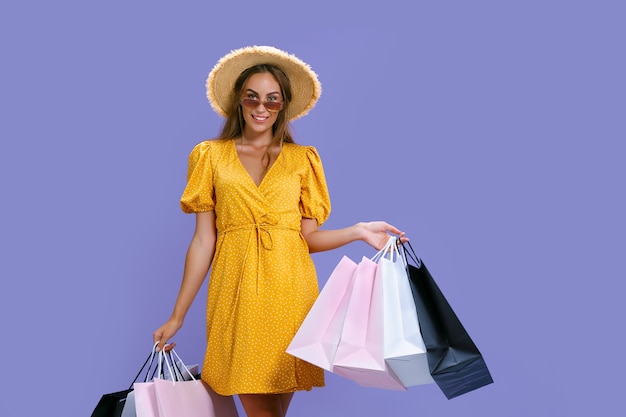 Happy woman in hat and sunglasses holds purchases while smiling at camera black friday big sales