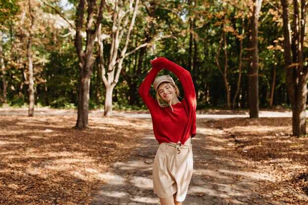 Happy woman having great time in the autumn park. Smiling blonde posing amoung fallen leaves.