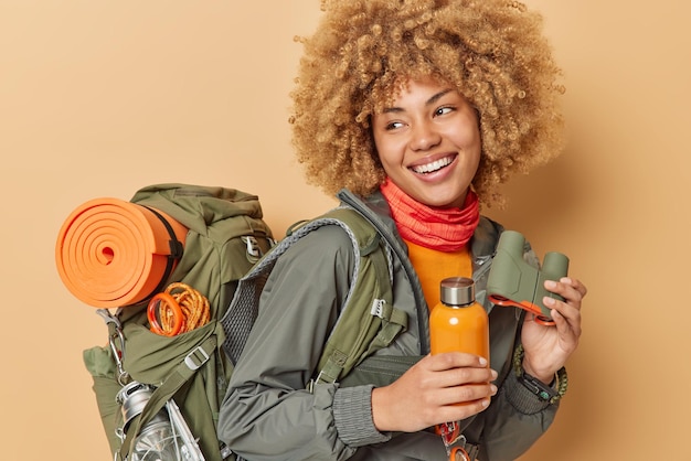 L'escursionista donna felice si diverte in campeggio porta un grande zaino tiene una bottiglia con acqua fresca e il binocolo andando a scalare la montagna esplora nuovi posti conduce uno stile di vita attivo guarda con gioia lontano