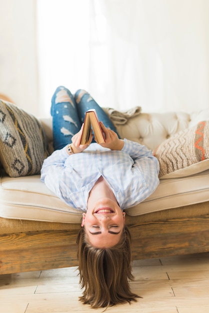 Happy woman holding book while lying on sofa