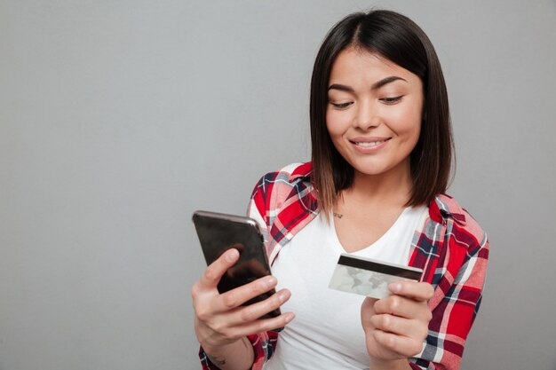 Happy woman holding credit card and using mobile phone