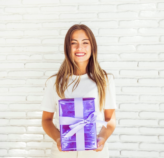 Happy woman holding gift box against brick wall