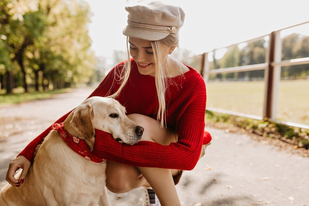 가 공원에서 그녀의 강아지를 부드럽게 잡고 행복 한 여자. 야외 애완 동물과 함께 좋은 시간을 보내고 사랑스러운 금발 소녀.