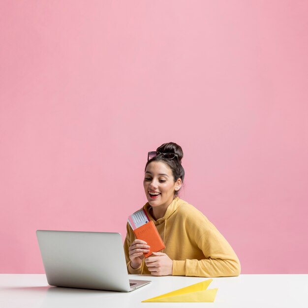 Happy woman holding her passport while looking on her laptop