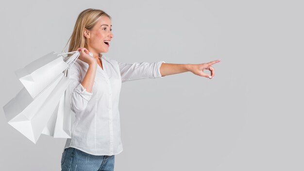 Happy woman holding shopping bags and pointing to possible store sale