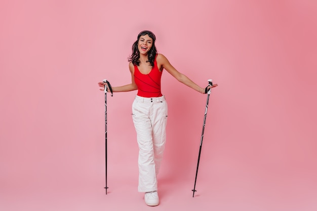 Happy woman holding ski poles on pink background