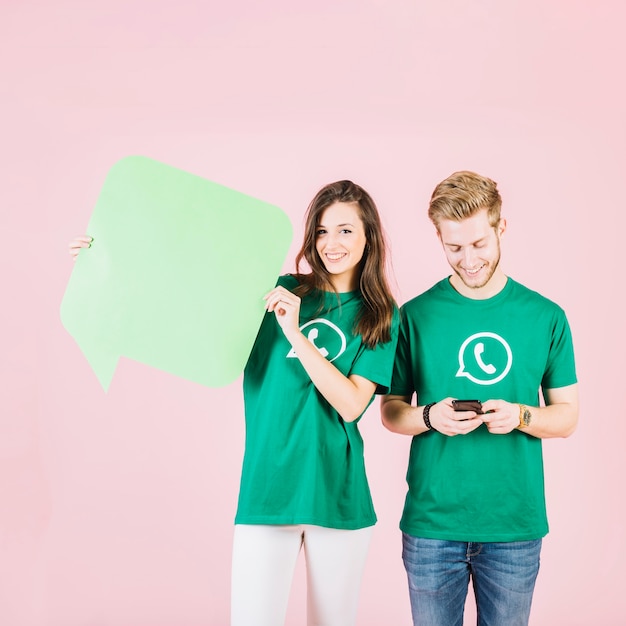 Happy woman holding speech bubble beside man using smartphone