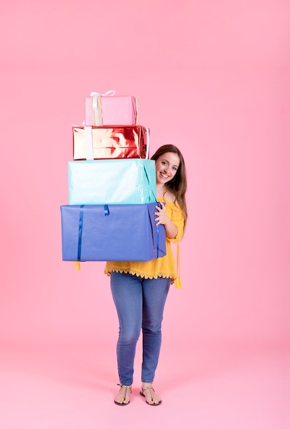 Free photo happy woman holding stack of colorful presents against pink backdrop