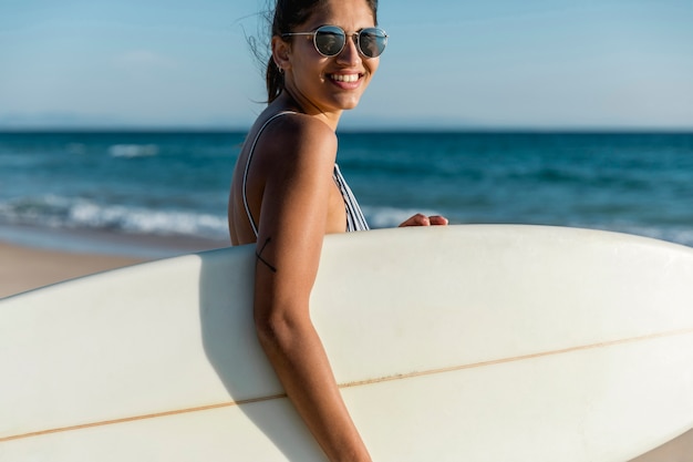 Free photo happy woman holding surfboard on shore