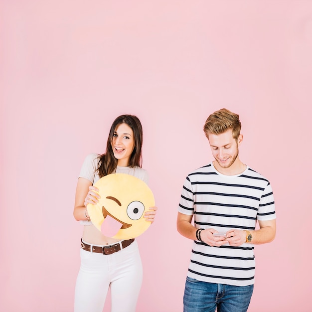 Happy woman holding winking eye emoji near her friend with cellphone