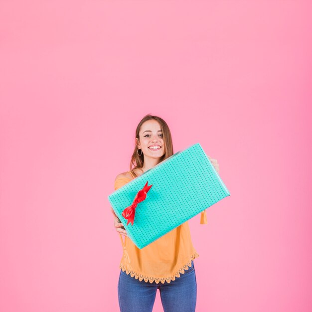 Happy woman holding wrapped gift box against pink background