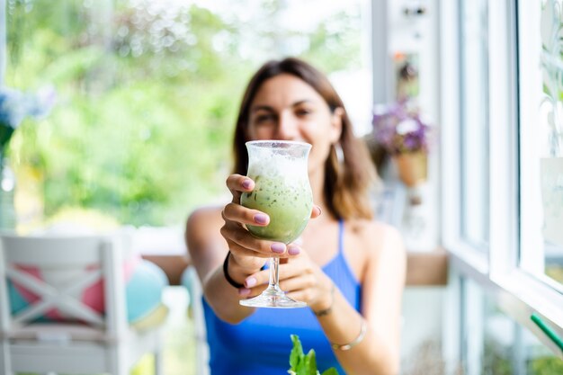 Happy woman holds japanese matcha green tea with ice in glass in cafe Female with healthy antioxidant beverage in summer cute cafe