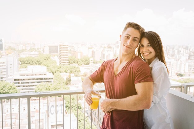 Happy woman hugging man with juice glass on balcony