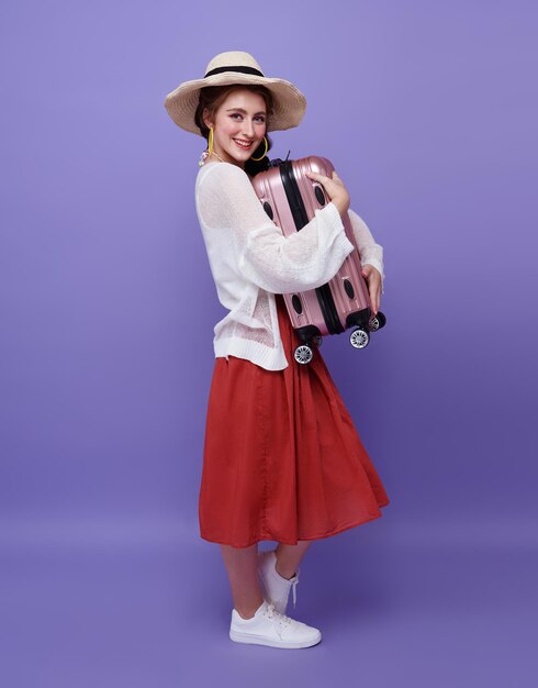 Happy woman hugging suitcase on purple background Tourist girl having cheerful holiday trip