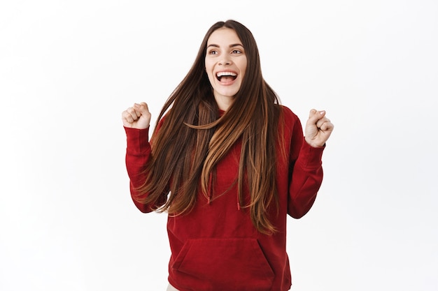 Donna felice che salta dalla gioia e dal trionfo, raggiunge l'obiettivo di successo, guardando da parte e urlando di felicità, celebra la vittoria, vincendo qualcosa, muro bianco