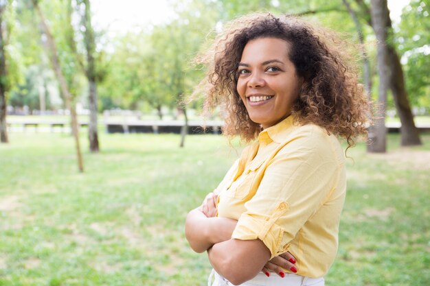 Happy woman keeping arms crossed and posing at camera in park