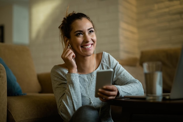 Foto gratuita donna felice che ascolta musica con gli auricolari mentre si utilizza il telefono cellulare a casa