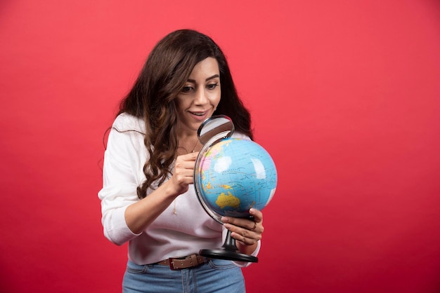 Happy woman looking at globe with magnifying glass. High quality photo