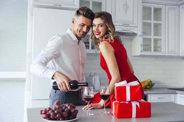 Happy woman looking while her man pouring wine into glasses at home