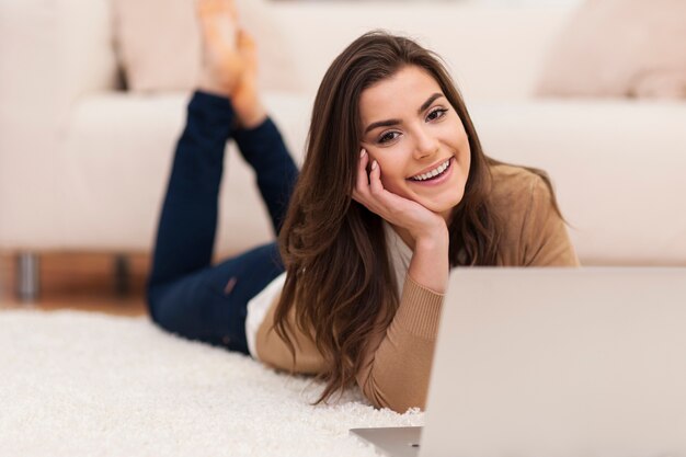 Happy woman lying down on carpet with laptop