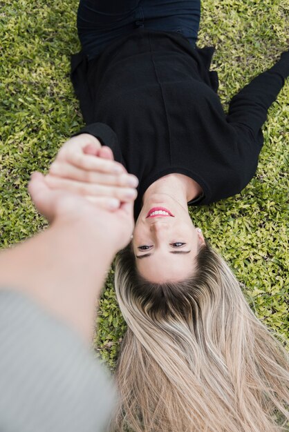 Happy woman lying in park holding man's hand