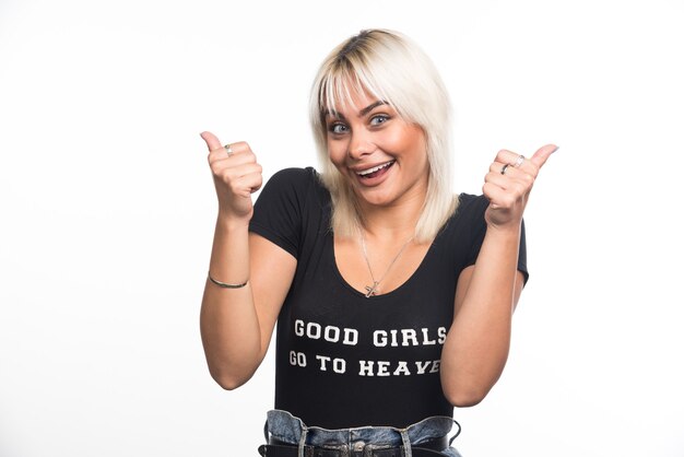 Happy woman making thumbs up signs on white wall.