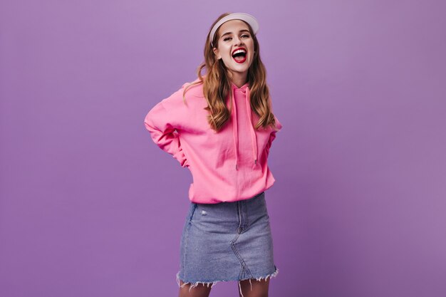 Happy woman in pink outfit and cap smiling on purple wall