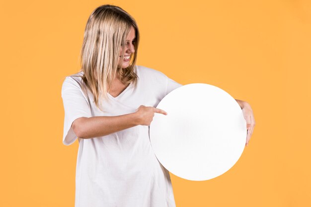 Happy woman pointing at white blank circular frame over yellow background