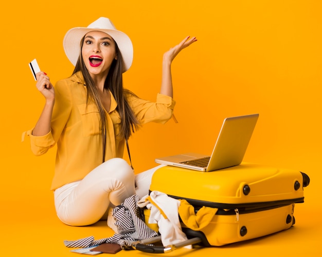 Happy woman posing next to luggage while holding credit card