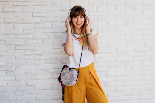Happy woman posing over white brick wall with earphones.