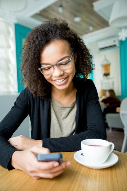 Happy woman reading message on cellphone in cafe