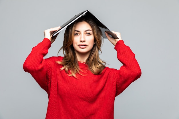 Happy woman in red sweater holding laptop above her head like a roof over gray wall.