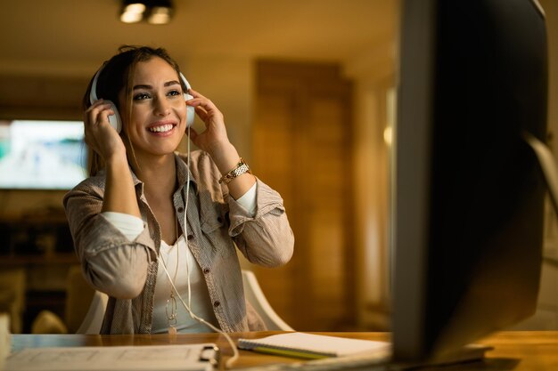 Happy woman relaxing in the evening while wearing headphones and surfing the net on computer at night