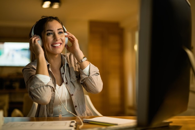 Happy woman relaxing in the evening while wearing headphones and surfing the net on computer at night