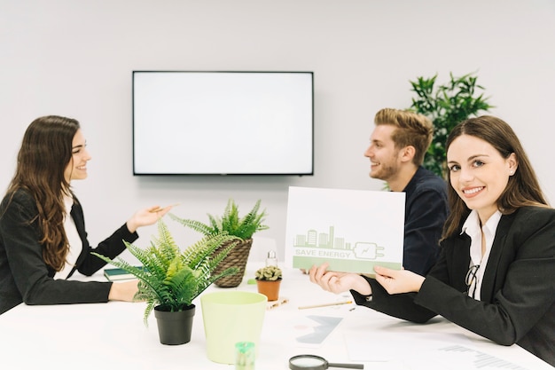 Foto gratuita donna felice che mostra concetto economizzatore d'energia su carta in ufficio