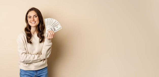 Free photo happy woman showing money cash and smiling pleased concept of microcredit and shopping standing over