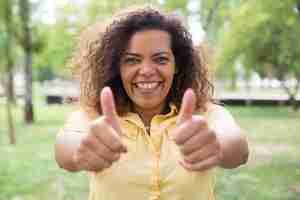 Free photo happy woman showing thumbs up and posing at camera in park