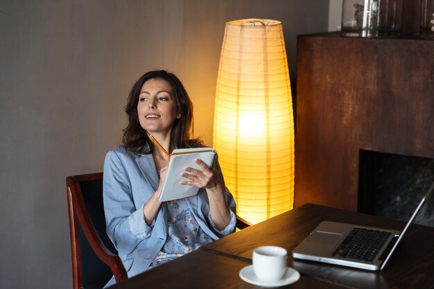 Happy woman sitting indoors writing notes.